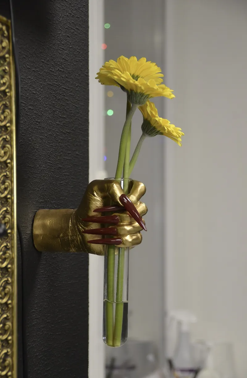 Zeltīta roka ar gariem nagiem tur dzeltenas gerberas