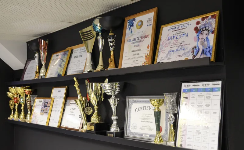 Manikīra konkursu kausi un diplomi plauktā